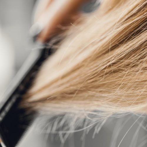Girl combing blonde hair with a brush. Closeup